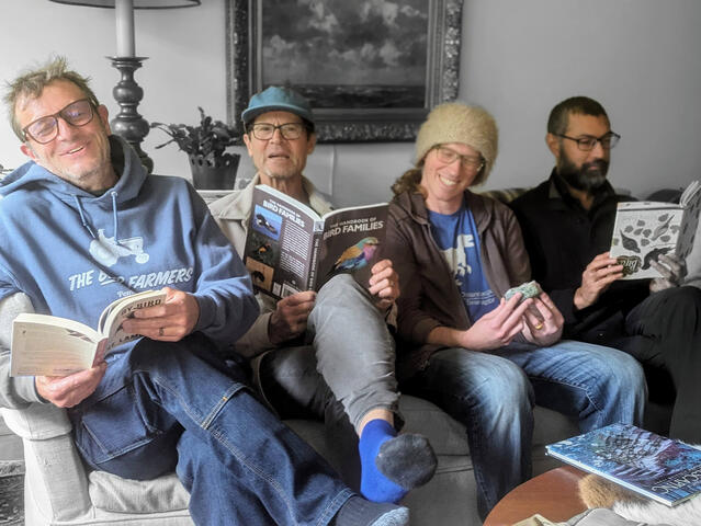 4 men sitting on a couch pretending to read books.